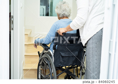 Caregiver help asian or elderly old woman sitting wheelchair support up the stairs in home. 84060245