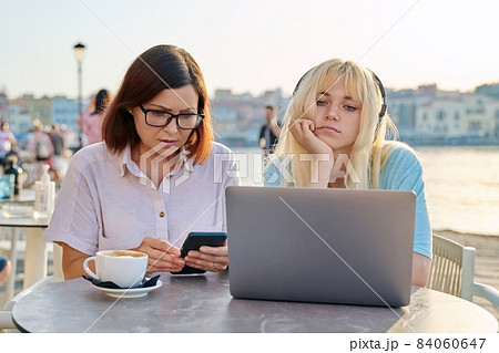 Serious mother and teenage daughter together in outdoor cafe looking at laptop 84060647
