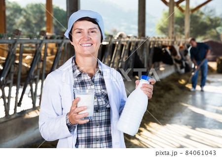 farmer in white robe posing background of cows in stall with milk 84061043