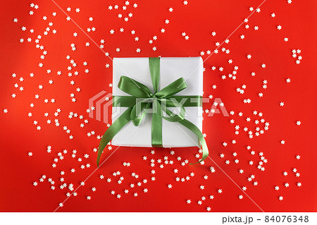 Gift box wrapped in white paper with a mint blue bow on festive crimson background with many snowflakes. Copyspace for your text. Flat lay style. Christmas, New Year or birthday celebration concept Gift box wrapped in white paper with a mint blue bow on festive crimson background with many snowflakes. Copyspace for your text. Flat lay style. Christmas, New Year or birthday celebration concept 84076348