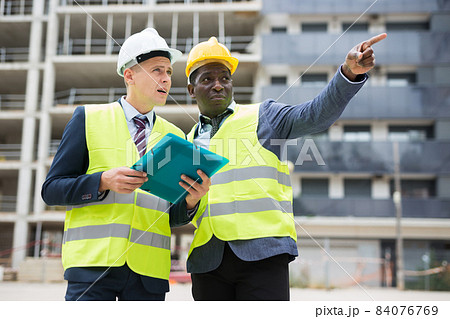 African-american engineer discussing a construction plan with a colleague shows him something 84076769