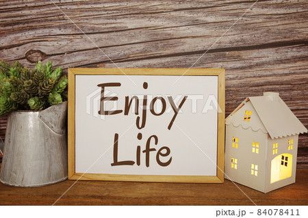 Blackboard with the text ENJOY LIFE decorate with artificial plant in watering plant and LED candle in house lantern on wooden background 84078411