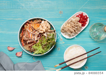 Korean cuisine or Asian . Crystal noodles with beef, vegetables and oyster mushrooms. Close-up, on a blue wooden background, with ingredients for cooking Korean cuisine or Asian . Crystal noodles with beef, vegetables and oyster mushrooms. Close-up, on a blue wooden background, with ingredients for cooking 84080354