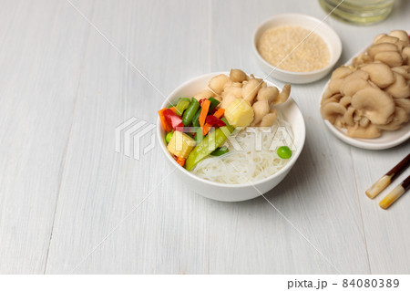 Bowl with funchosa, vegetables and oyster mushrooms. On a light wooden background, horizontal with space Bowl with funchosa, vegetables and oyster mushrooms. On a light wooden background, horizontal with space 84080389