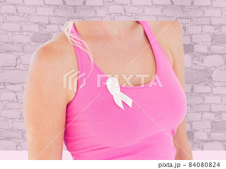 Mid section of woman wearing a pink ribbon on her sleeve against brick wall in background 84080824