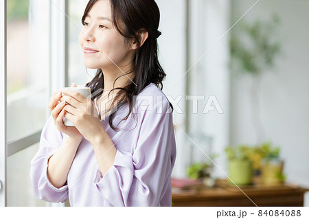 マグカップを持って窓辺に立つ女性 84084088