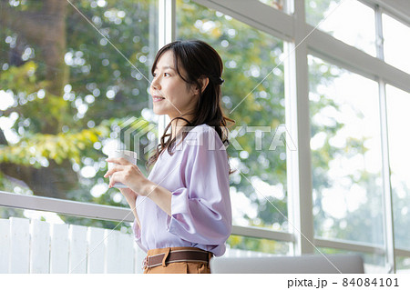 マグカップを持って窓辺に立つ女性 84084101