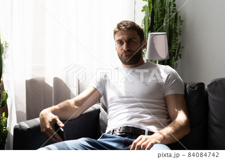 Sad thoughtful bearded man sitting on a sofa near window 84084742
