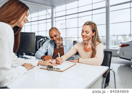 Beautiful young couple signs documents at car dealership showroom 84084809