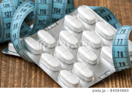 Weight loss pills in blister packs and measuring tape on wooden background 84084860