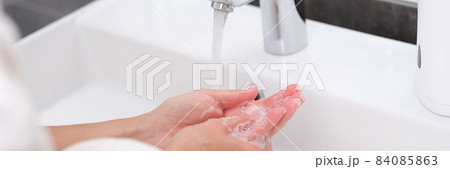 Woman washing her hands under water from tap in bathroom closeup Woman washing her hands under water from tap in bathroom closeup 84085863