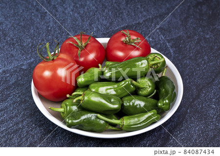 Green peppers and red tomatoes on a plate on a piece of slate. Healthy food concept Green peppers and red tomatoes on a plate on a piece of slate. Healthy food concept 84087434