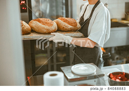 Woman holds tray with large breads standing in spacious craft bakery 84088883