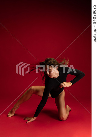 Portrait of emotional young flexible contemp dancer, ballerina dancing isolated on dark red background. Art, beauty, inspiration concept. 84089035