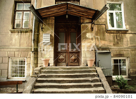 Old weathered brown entrance door under a hood with stairs 84090101