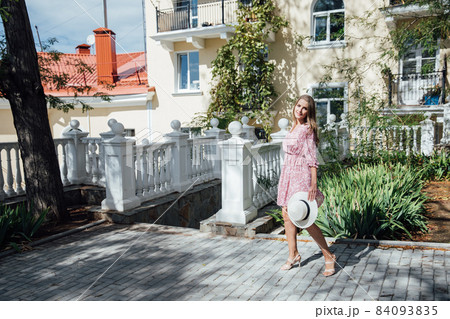 beautiful fashionable blonde woman in a hat and pink dress walking on the street 84093835
