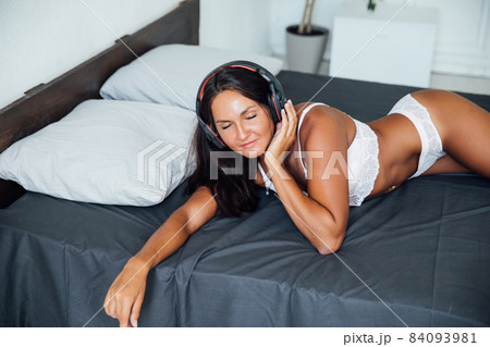 beautiful woman in lingerie listening to music in headphones on the bed in the bedroom 84093981