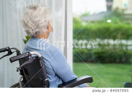 An elderly woman sitting on wheelchair looking out the window for waiting someone. Sadly, melancholy and depressed. 84097093
