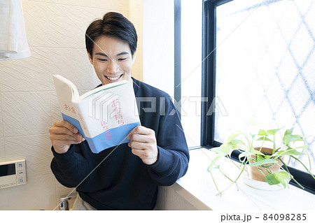 洗濯物を干した風呂場で「お金持ちになる話」という本を読む男性 84098285