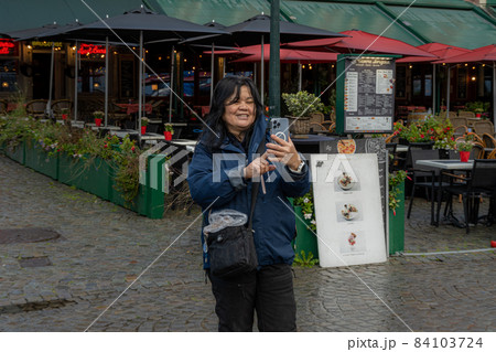 An Asian woman takes a selfie in front of a restaurant. Picture from the market square, Grote Markt, in Bruges, Belgium. An Asian woman takes a selfie in front of a restaurant. Picture from the market square, Grote Markt, in Bruges, Belgium. 84103724