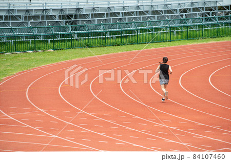 Back view of young athlete runner woman running in the running track in stadium. Running track is a rubberized artificial running surface for track and field athletics. 84107460