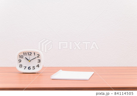 The notebook and the clock are on the table. 84114505