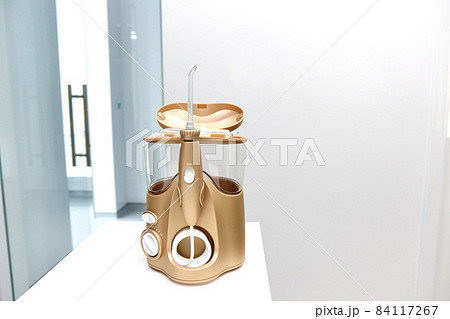 The dentist's golden sprinkler irrigator stands on a table on a bright white background in the dentist's office with the lid open and inside are different nozzles side view 84117267