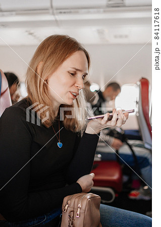 woman is records a voice message on the phone in a seat on board the plane. woman is records a voice message on the phone in a seat on board the plane. 84117618