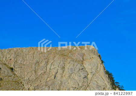 Half-divided view of a mountain naked peak over a precipice and a blue cloudless sky Half-divided view of a mountain naked peak over a precipice and a blue cloudless sky 84122997