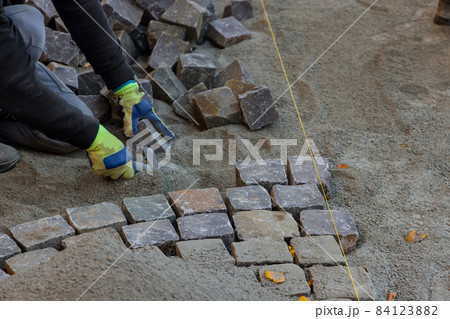 The road master in gloves lays paving stones in layers stone road by professional paver worker 84123882