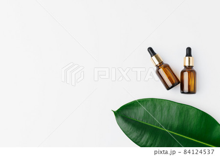 Essential oil in a small bottle with green leaf on white background 84124537