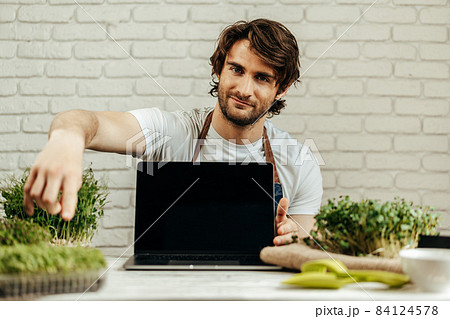 Man farmer shows black screen of laptop and sits at the table with sprouts Man farmer shows black screen of laptop and sits at the table with sprouts 84124578