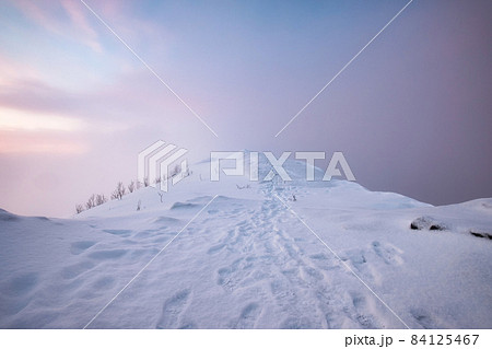 Snow covered mountain peak with footprint and colorful sky in blizzard on mount Segla at Senja island Snow covered mountain peak with footprint and colorful sky in blizzard on mount Segla at Senja island 84125467