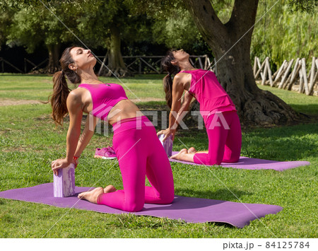 Two women practicing pilates or stretching with yoga block in park 84125784