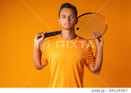 Studio shot of a young tennis player holding racket against orange background Studio shot of a young tennis player holding racket against orange background 84126367