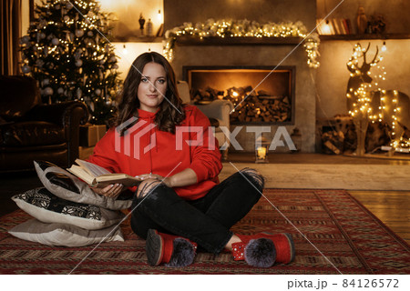 A young beautiful girl in a red sweater poses against the background of a New Year's interior. A young beautiful girl in a red sweater poses against the background of a New Year's interior. 84126572