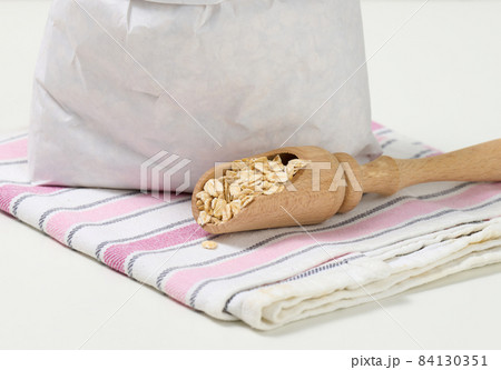 raw oatmeal in a white paper bag and a wooden spoon on a white table, breakfast porridge 84130351