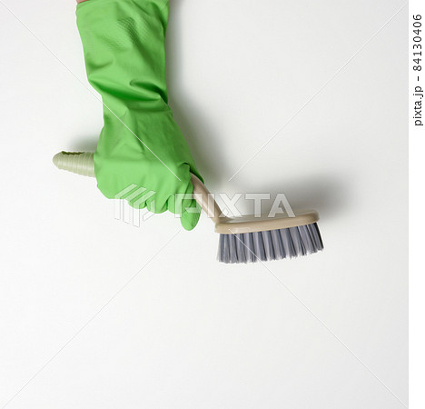 hand in a green rubber cleaning glove holds a plastic brush on a white background 84130406