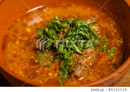 A bowl of beef vegetable soup garnished with dill and parsley. 84132114