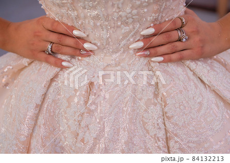 Close-up bride's dress with a beautifully embroidered pattern and hands on the waist with a beautiful manicure. Close-up bride's dress with a beautifully embroidered pattern and hands on the waist with a beautiful manicure. 84132213
