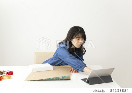ネットの動画を見ながら机でプレゼントの梱包をする若い女性 ネットの動画を見ながら机でプレゼントの梱包をする若い女性 84133884
