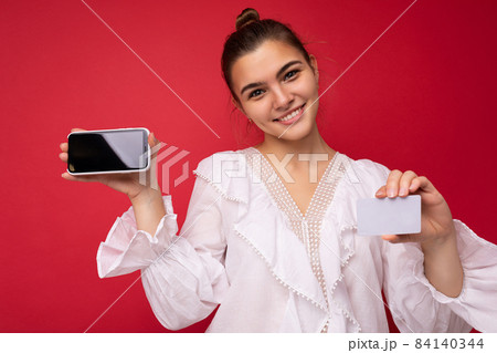 Portrait of positive cheerful fashionable woman in formalwear holding and showing mobile phone with 84140344