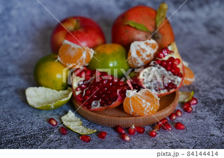 A pomegranate, whole and broken into pieces with other fruits, lies on a marble table A pomegranate, whole and broken into pieces with other fruits, lies on a marble table 84144414
