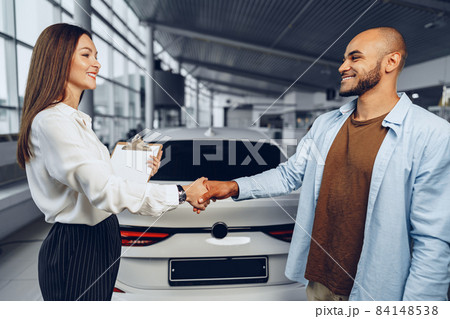 Woman car seller and man car buyer handshaking in car salon Woman car seller and man car buyer handshaking in car salon 84148538