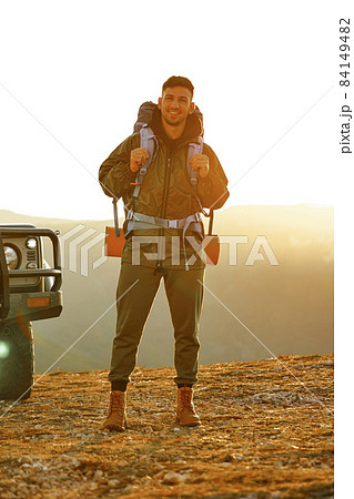 Portrait of a young traveler man in hiking equipment standing near his off-road car Portrait of a young traveler man in hiking equipment standing near his off-road car 84149482