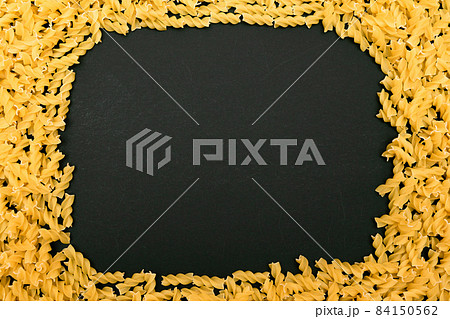 A Frame Made from Uncooked Fusilli Pasta Scattered on Black Table 84150562