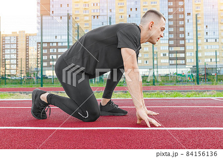 Athlete on the starting line of a stadium track preparing for a run. 84156136