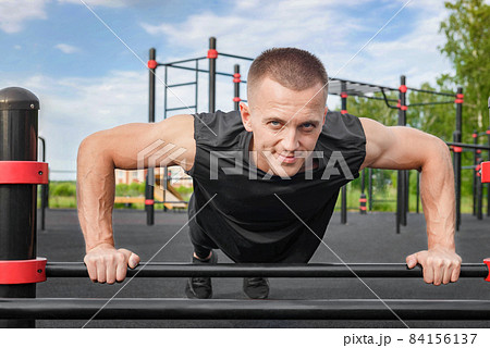 Young man doing push-up exercise on the street on an iron bar. 84156137