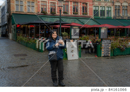 An Asian woman takes a selfie in front of a restaurant. Picture from the market square, Grote Markt, in Bruges, Belgium. An Asian woman takes a selfie in front of a restaurant. Picture from the market square, Grote Markt, in Bruges, Belgium. 84161066