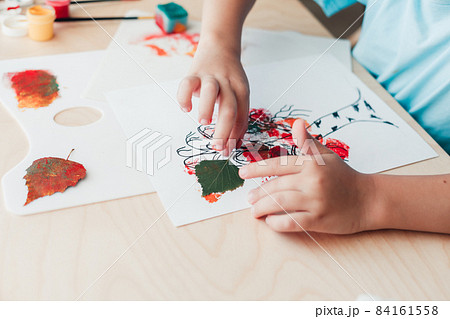 Cute child sitting at desk and making picture from dry birch leaves Cute child sitting at desk and making picture from dry birch leaves 84161558